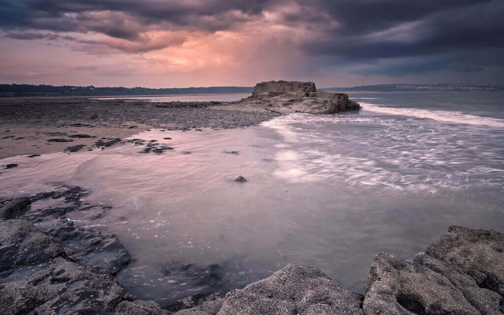 Een regenbui, bij de rotsen aan de kust, tijdens zonsondergang bij Porthcawl.