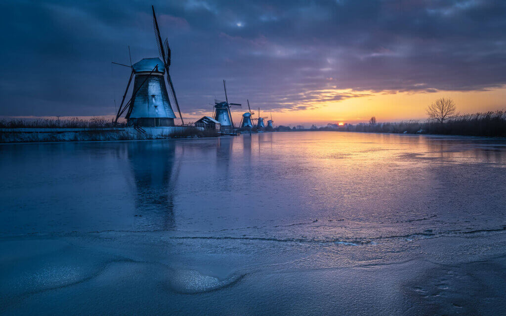 Winterse omstandigheden bij zonsopkomst, aan een bevroren rivier en met sneeuw bedekte molens, op Kinderdijk.