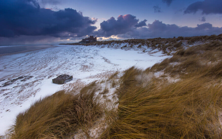 Op een vroege ochtend, tijdens zonsopkomst, lag er sneeuw op het strand bij Bamburgh castle.