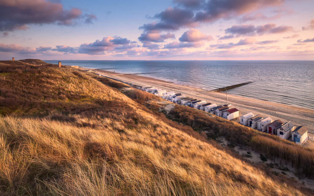 Net voordat de zon ondergaat, kleurt hij de duinen van bruin naar goud. De wolken kleuren in zachte pasteltinten mee boven de kust van Dishoek.