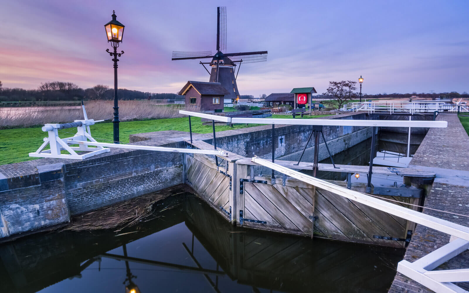 De molen bij de Zevenhuizense Verlaat tijdens zonsondergang. De lichten van de sluis zijn net aangesprongen.
