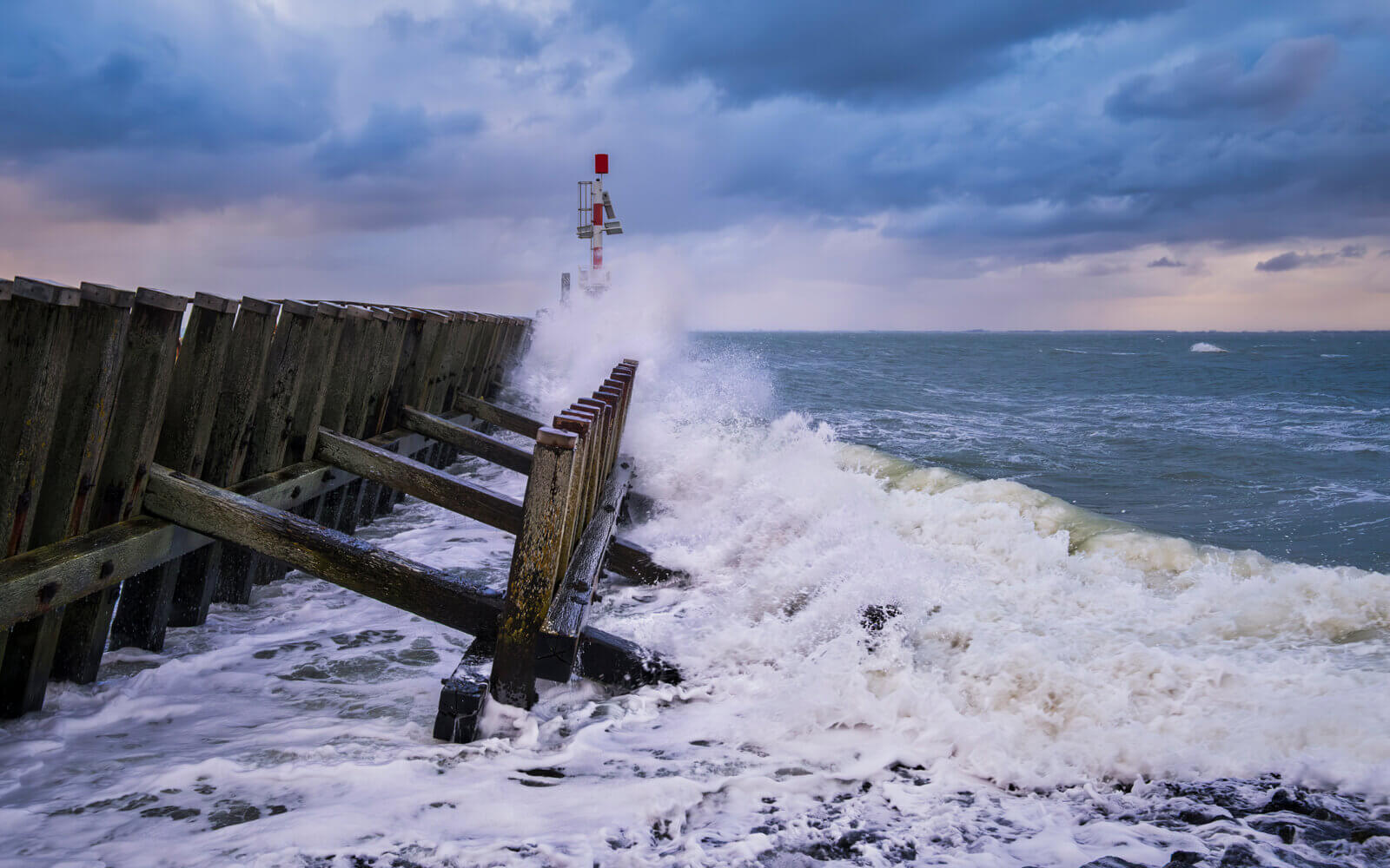 Een golf spat uiteen bij de havenboei steiger bij de haven van Vlissingen. Een stormachtige ochtend aan de Westerschelde in Zeeland.