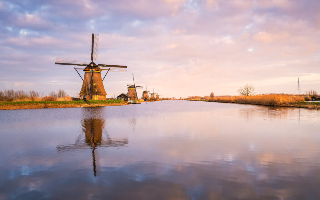 Prachtige, vredige en kalme lentezonsondergang bij de windmolens van Kinderdijk. Mooie weerspiegeling van de windmolen en de wolken in de beek.